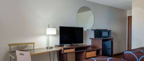 A hotel room with a desk, television, microwave, refrigerator, and two beds with patterned bedding.