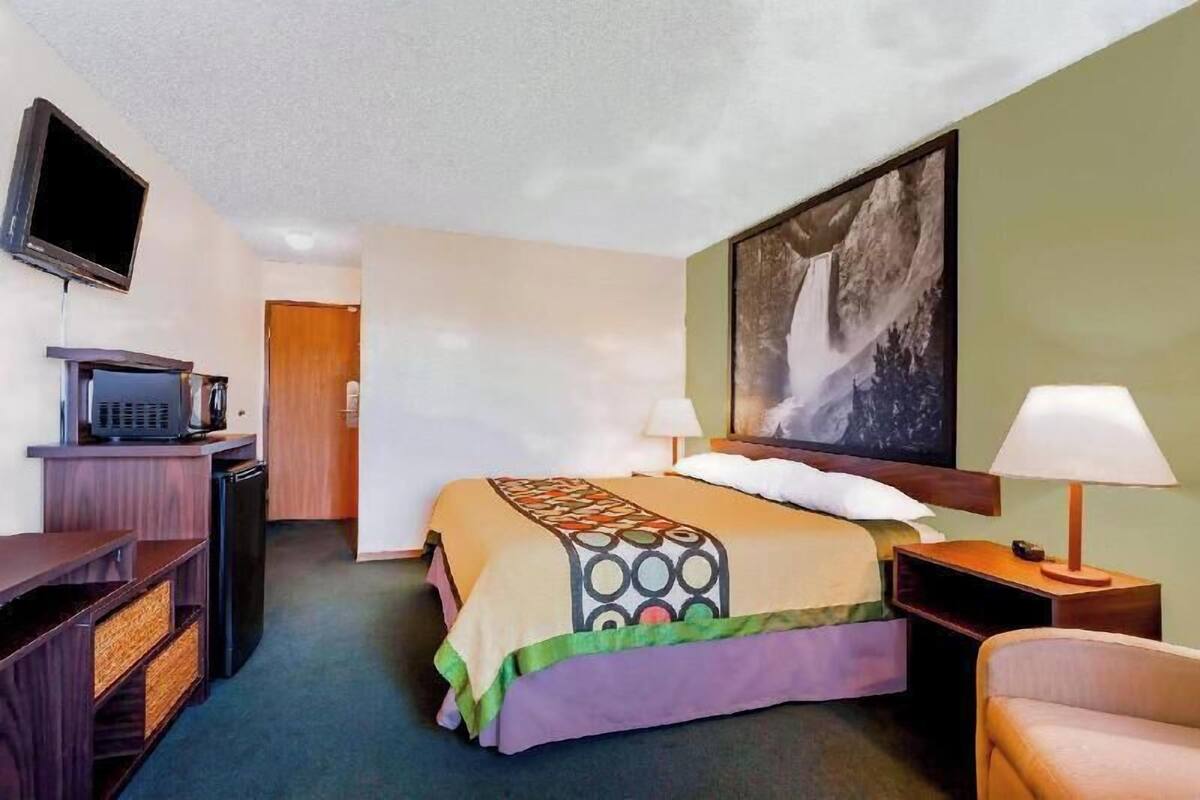 A hotel room with a bed, a television, a desk with a computer, a lamp, and a painting on the wall.