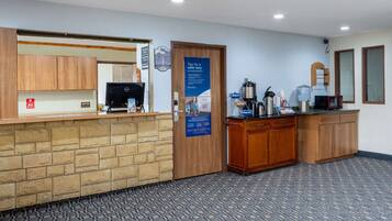 A reception area with a stone counter, wooden cabinets, a coffee station, and a door with a safety tip poster.