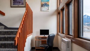 A corner office with a desk, computer, and chair, a staircase with patterned carpet, and a window with a mountain view. - Super 8 by Wyndham Livingston Yellowstone (Livingston)
