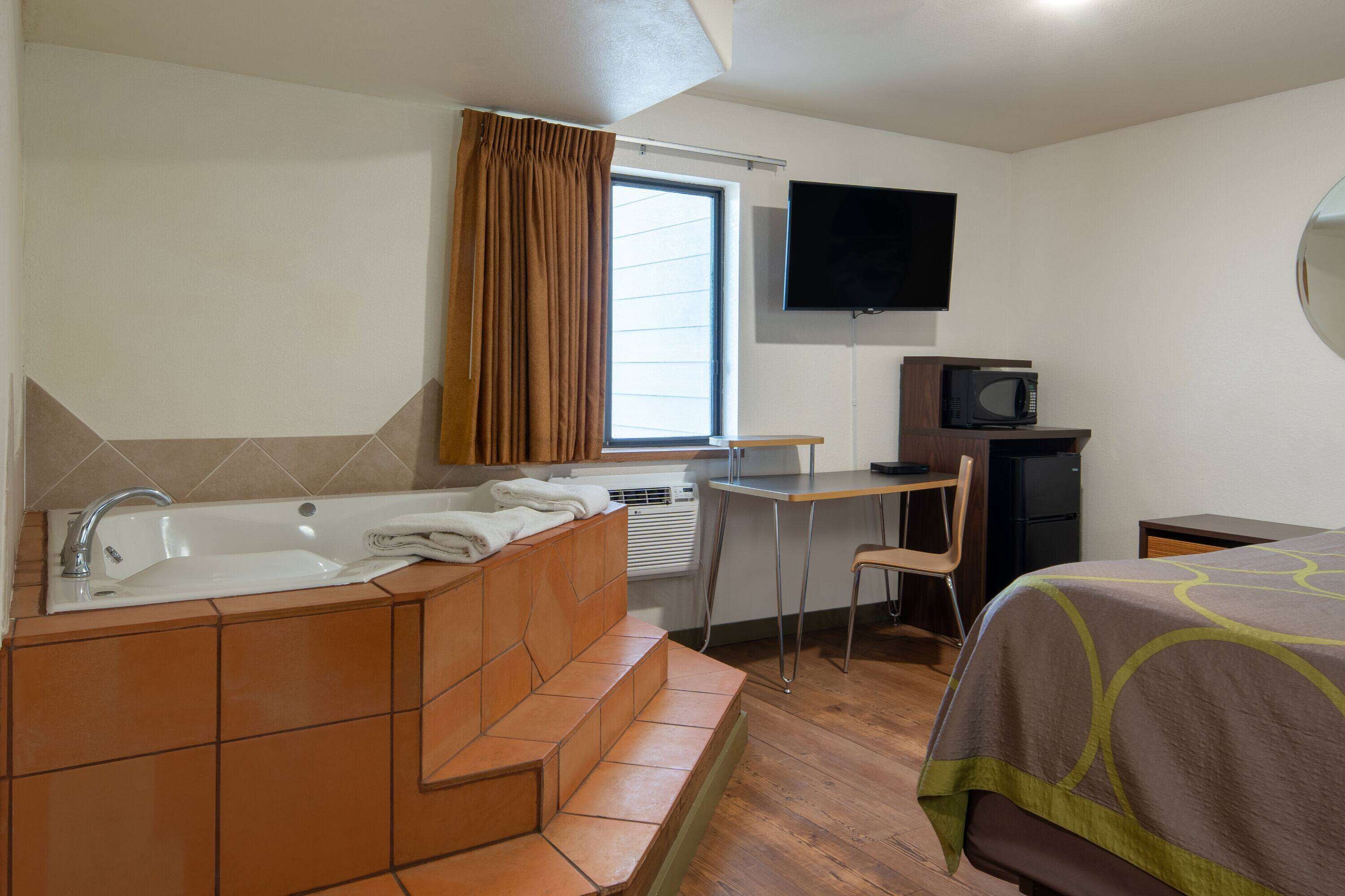 Ett hotellrum med badkar, skrivbord, tv och en säng.