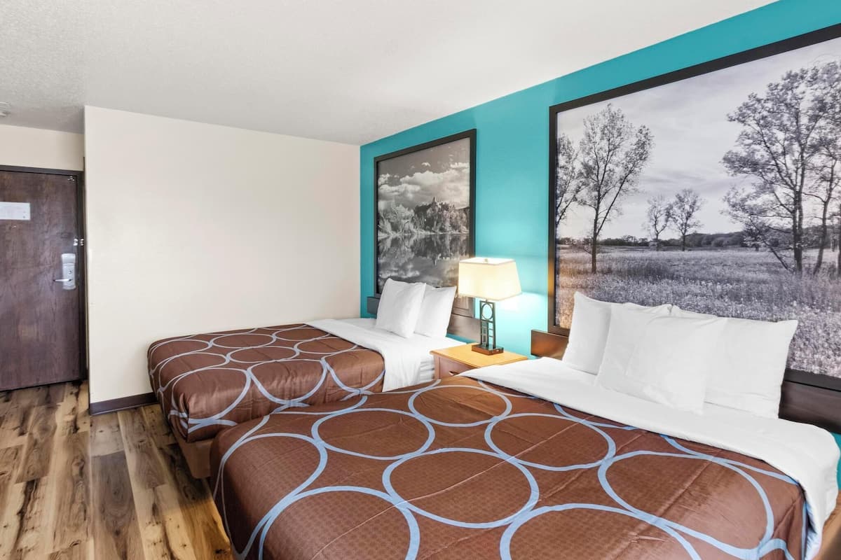 A hotel room with a double bed, a nightstand with a lamp, and a large landscape painting on the wall.