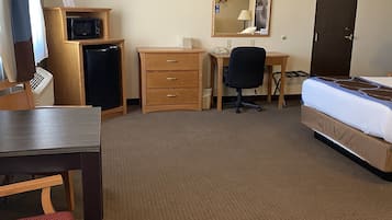 A hotel room with a bed, desk, chair, dresser, microwave, refrigerator, and a door.
