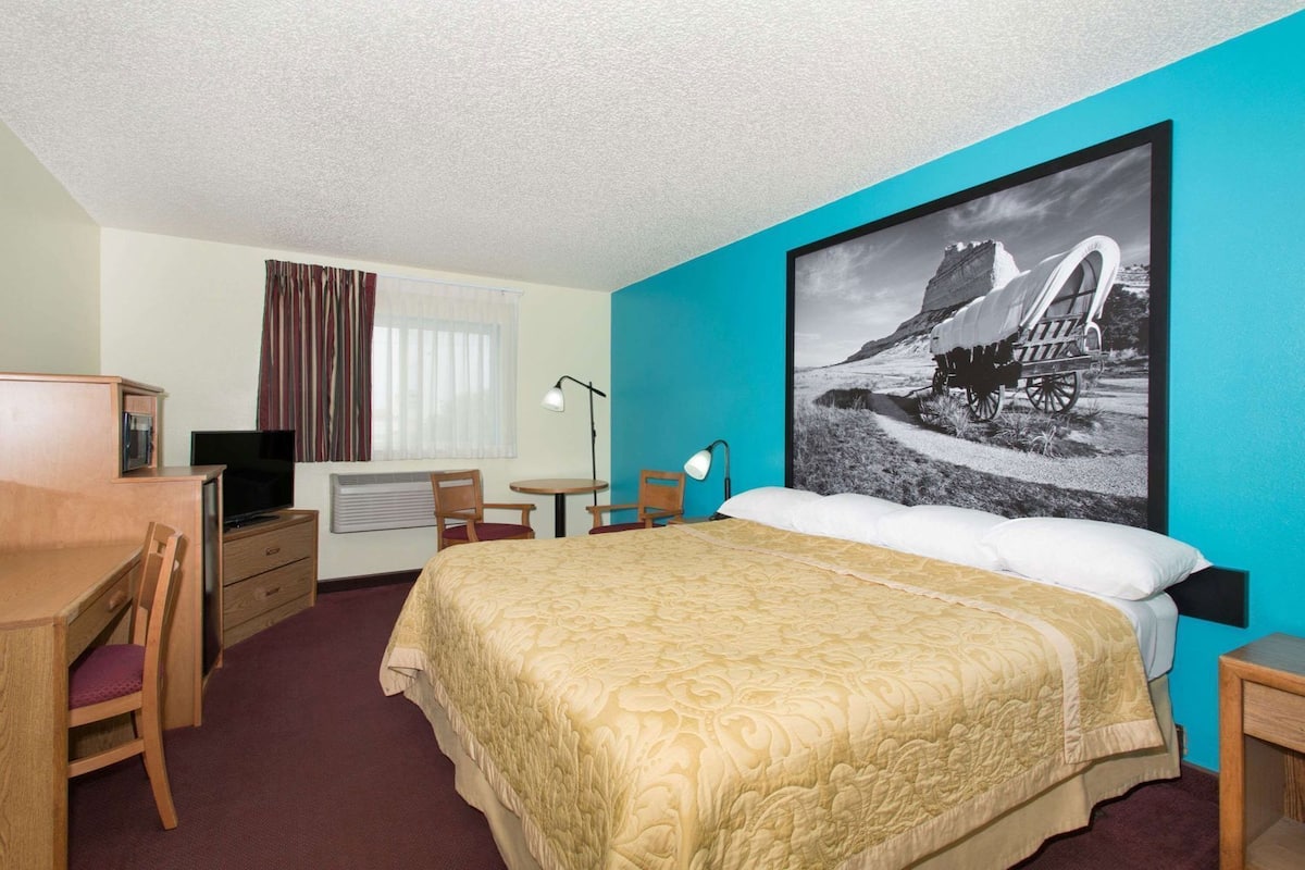 A hotel room with a bed, desk, chair, TV, and a large wall-mounted picture.