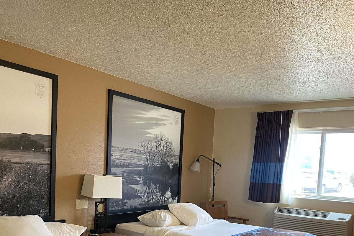 A hotel room with two beds, a large framed picture, a lamp, and a window with curtains.