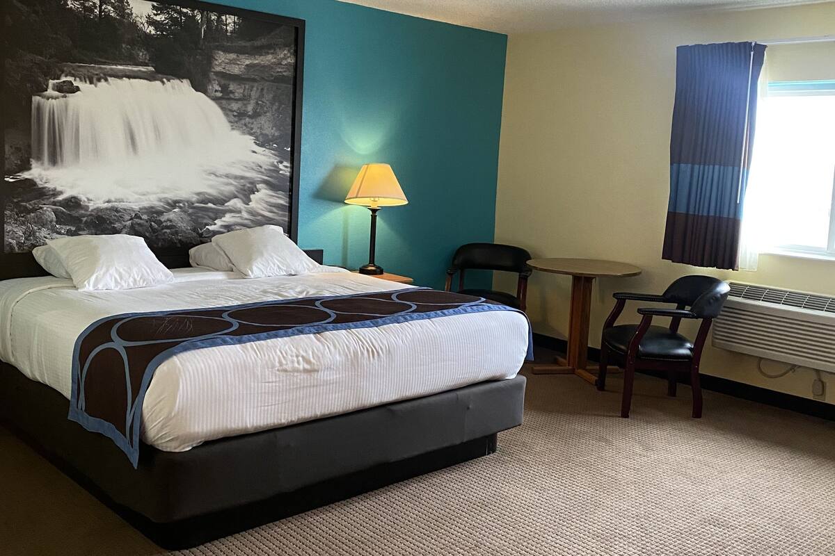 A hotel room with a large bed, a desk, a chair, a lamp, and a large wall painting.