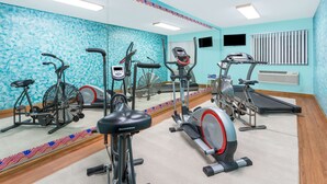 Une salle de sport équipée de divers appareils d’exercice, dotée d’un grand miroir et d’une fenêtre avec des stores.