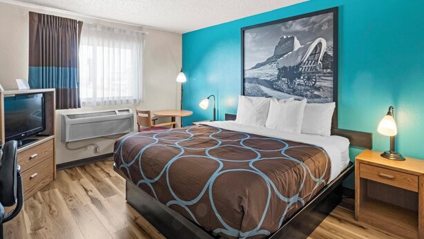 Une chambre d’hôtel équipée d’un lit, d’un bureau, d’une chaise, d’une télévision, d’un climatiseur et d’une fenêtre avec des rideaux.