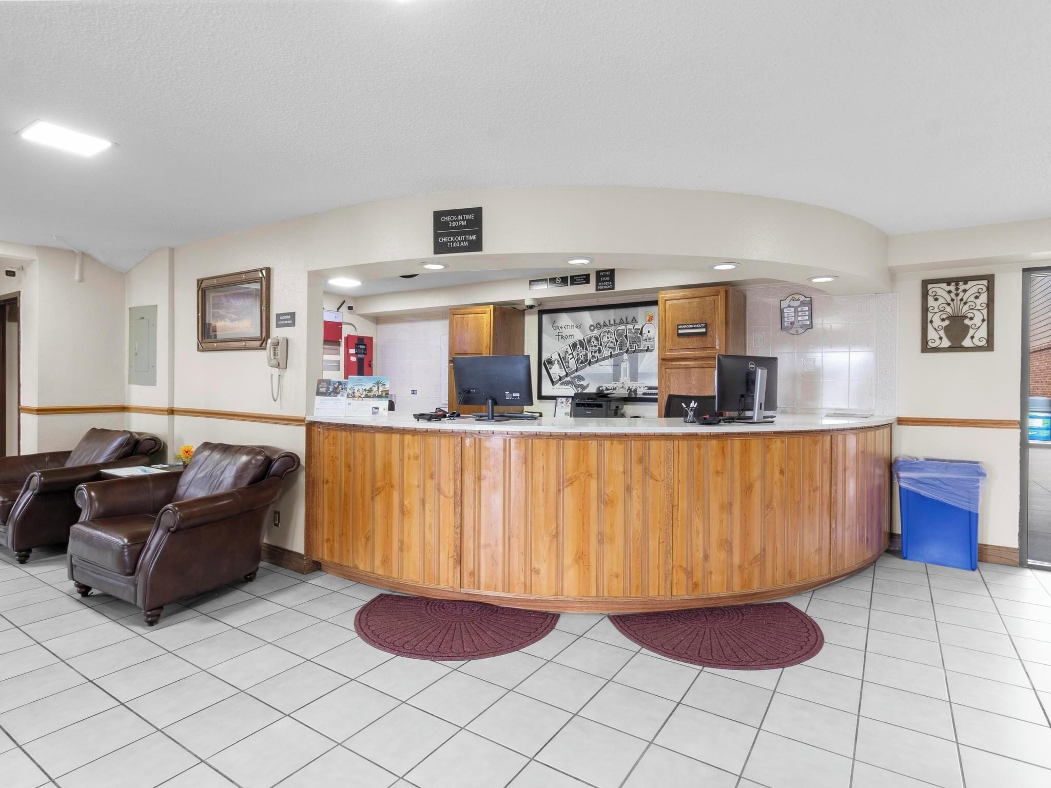 A reception area with a wooden counter, two computer monitors, a telephone, and a blue trash bin.