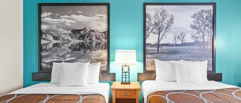 Habitación de hotel con dos camas, una mesita de noche y dos grandes cuadros de paisajes en las paredes.