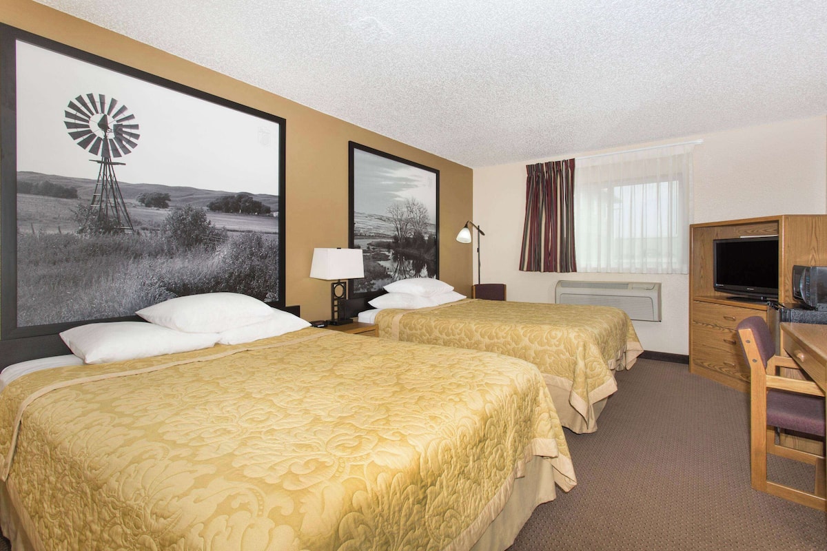 A hotel room with two beds, a desk, a television, and a window with curtains.
