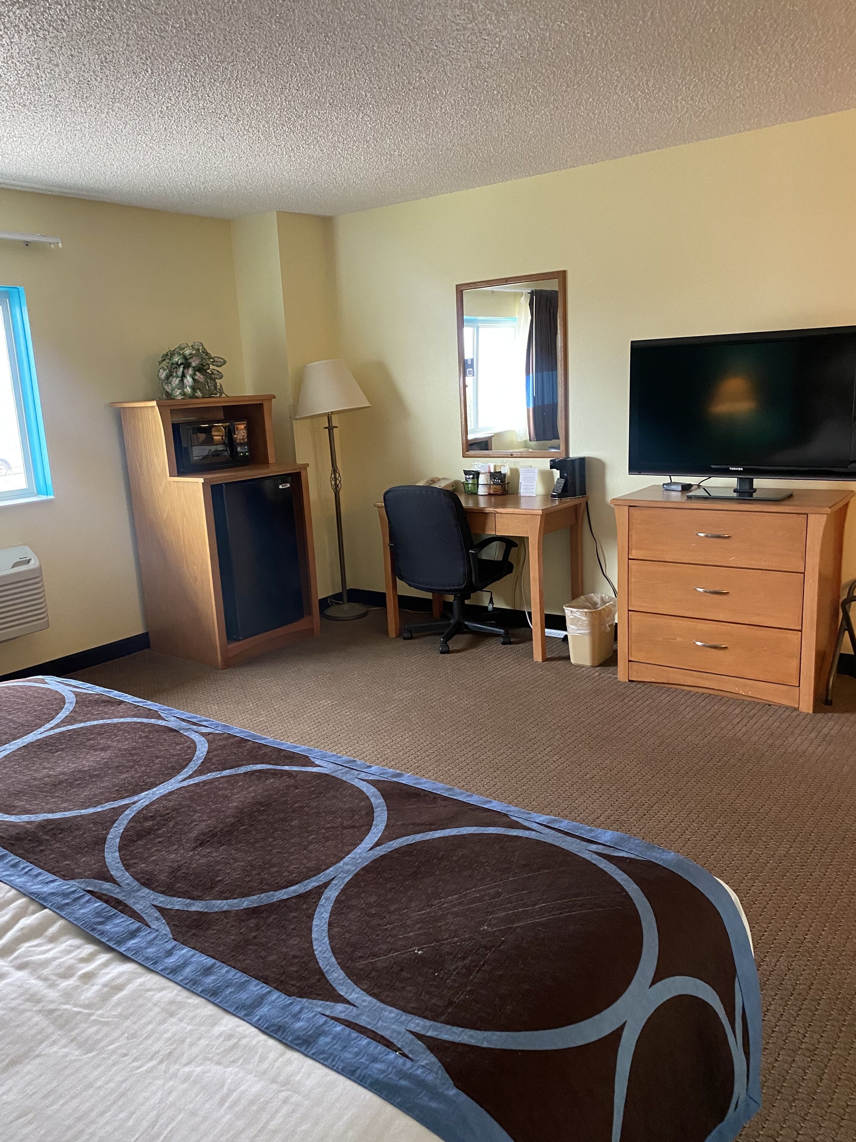 A hotel room with a bed, desk, television, and a minibar.