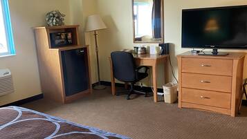 A hotel room with a bed, desk, television, and a minibar.