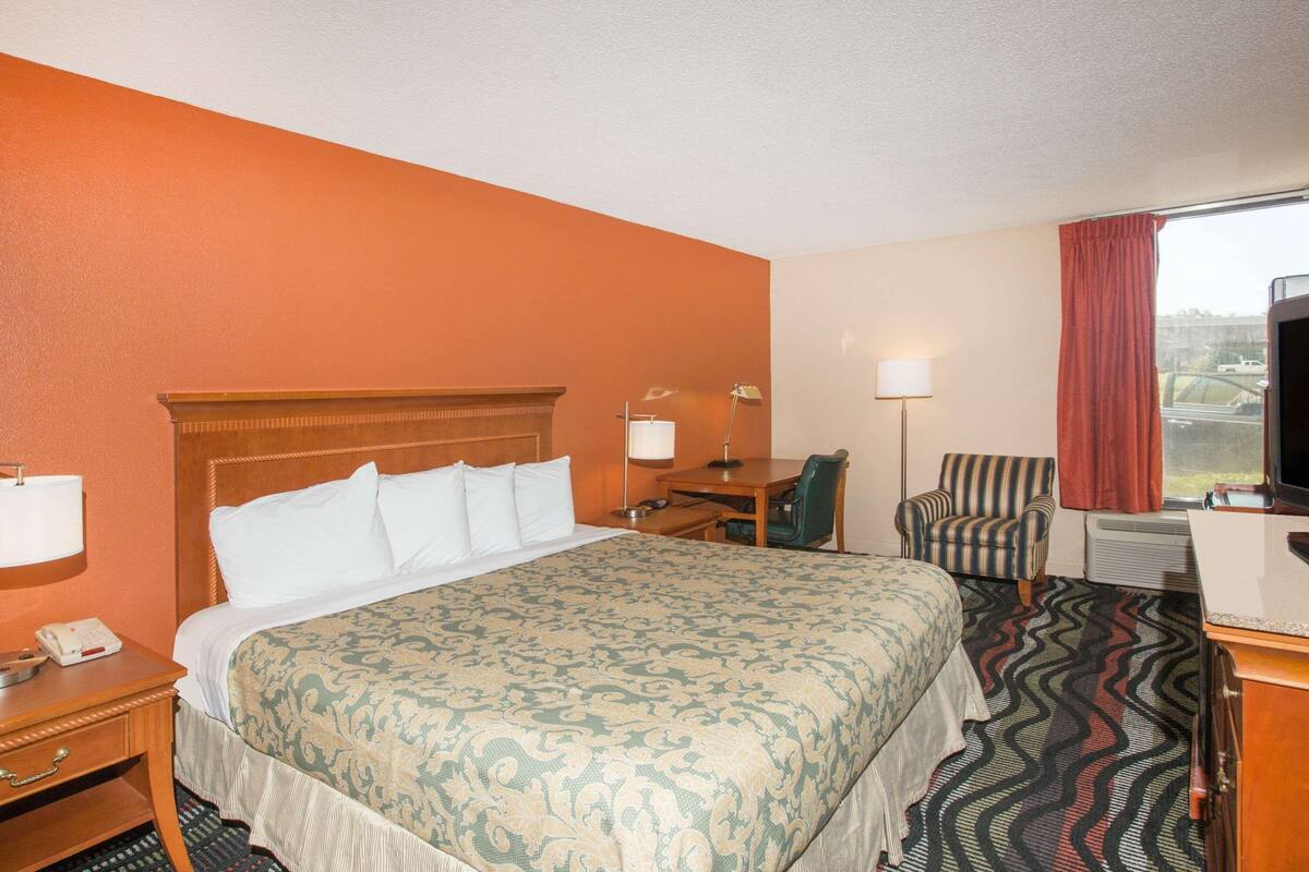 A hotel room with a bed, desk, chair, and a television.