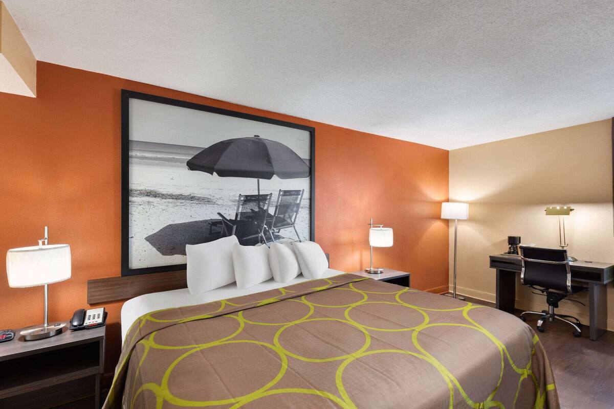 A hotel room with a bed, a desk, a chair, a phone, and a lamp.