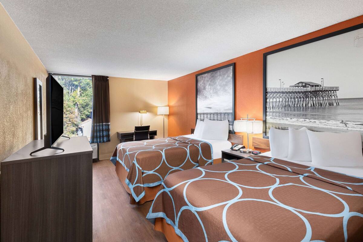 A hotel room with a bed, a desk, a chair, a TV, and a large window with a view of a pier.