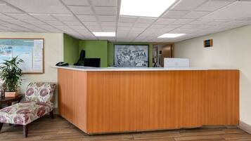 A reception area with a wooden desk, a green wall, a bulletin board, and a potted plant.