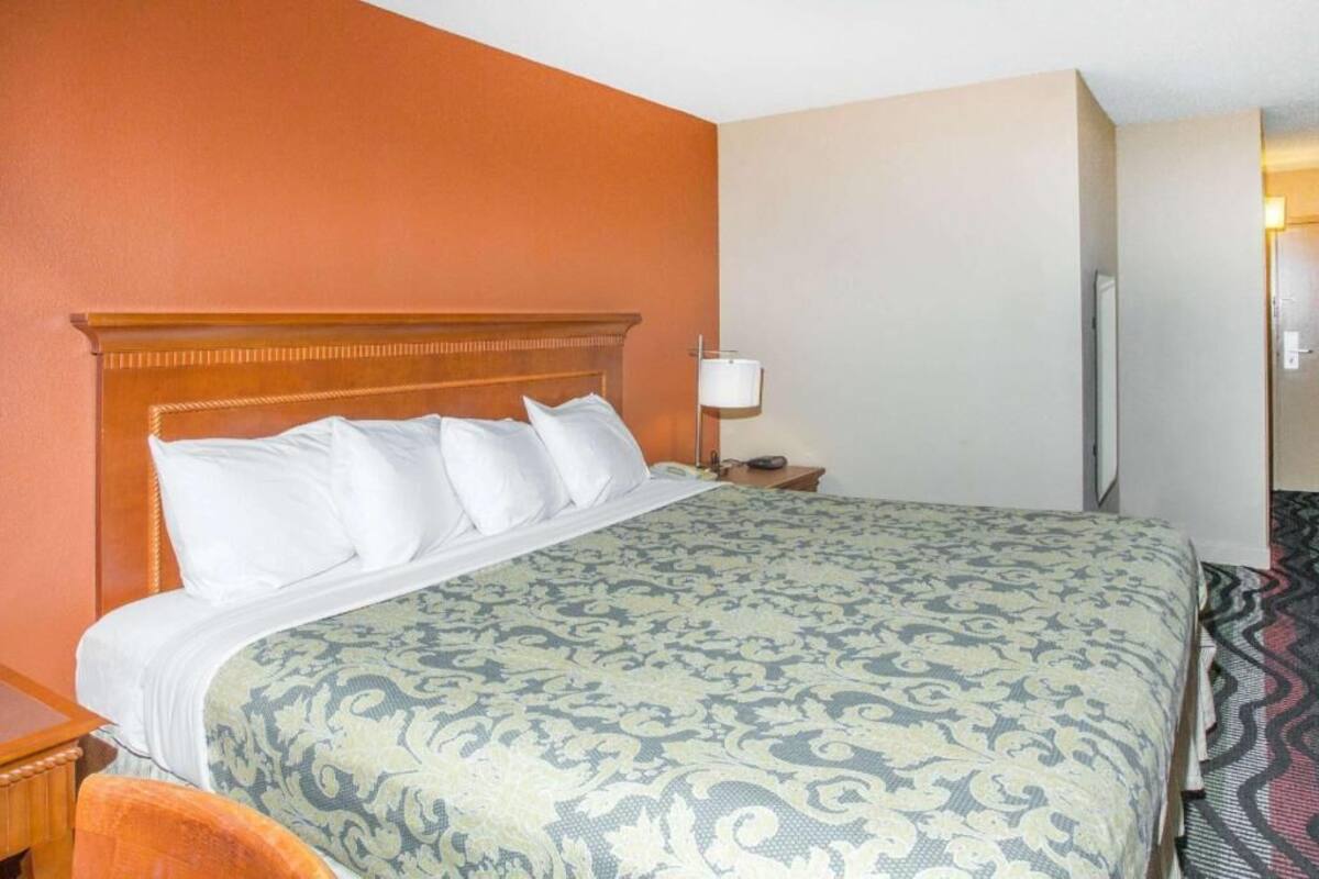 A hotel room with a bed, a nightstand, a lamp, and a chair.