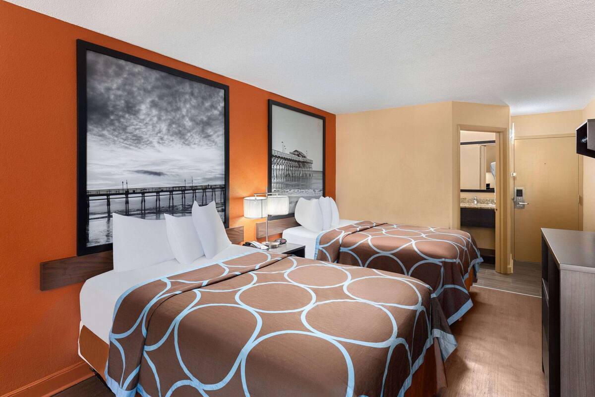 A hotel room with two beds, a desk, a chair, a TV, and a large window with a view of a pier.
