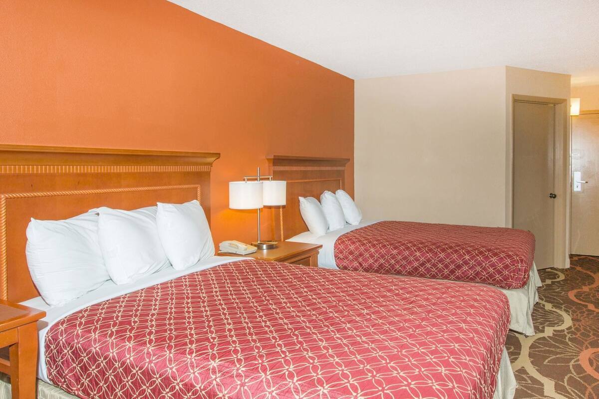 A hotel room with two beds, a nightstand with a lamp, and a door.