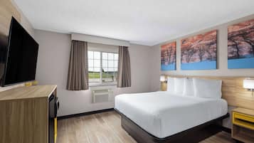 Quarto de hotel com cama, televisão, escrivaninha e janela com cortinas.