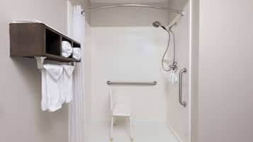 A shower area with a white chair, a shelf with towels, and a grab bar.