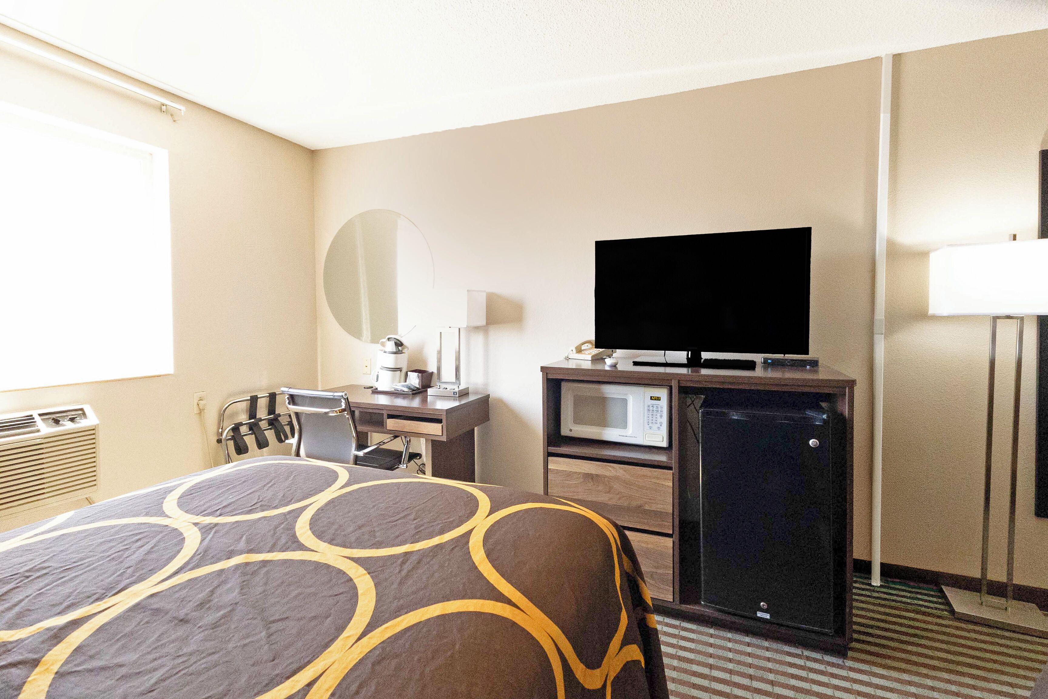 Una habitación de hotel con una cama, un escritorio con computadora, televisión, microondas y refrigerador.
