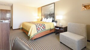A hotel room with a bed, a chair, a desk, and a large painting on the wall.