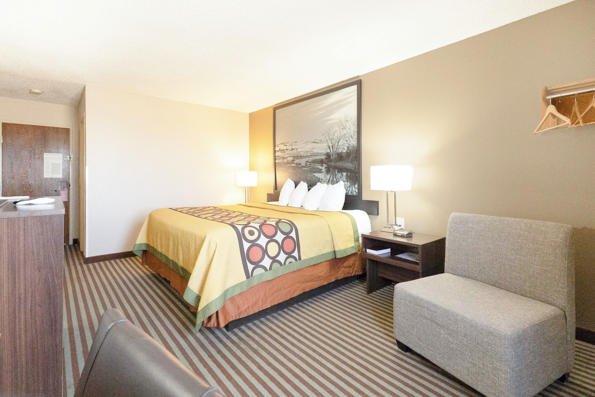 A hotel room with a bed, a chair, a desk, and a large painting on the wall.