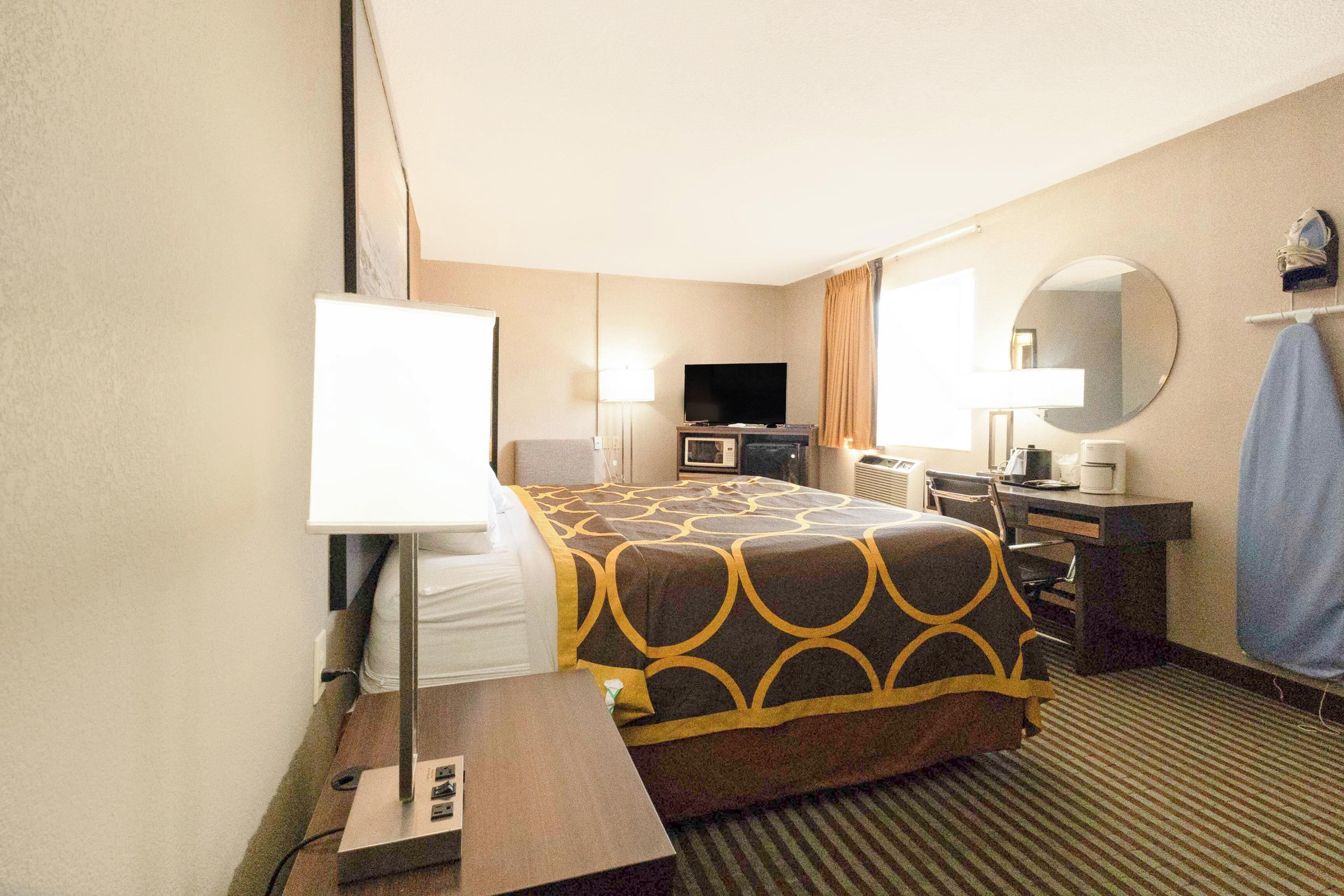 A hotel room with a bed, a desk, a television, a mirror, and a window.
