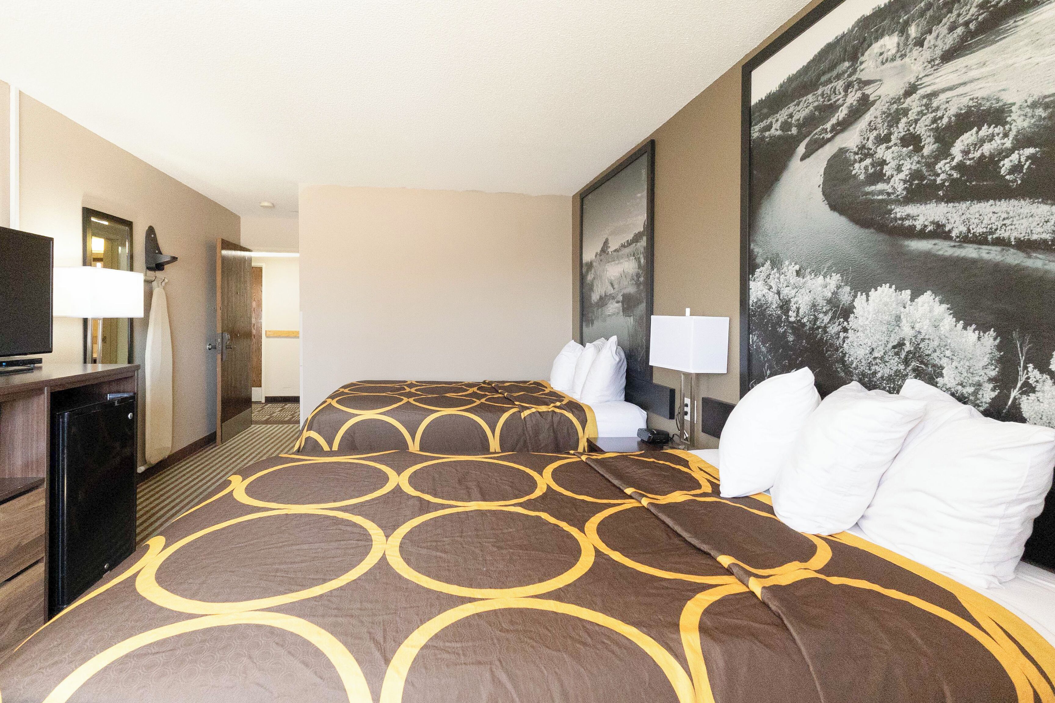 A hotel room with a bed, a TV, a desk, and a large painting on the wall.