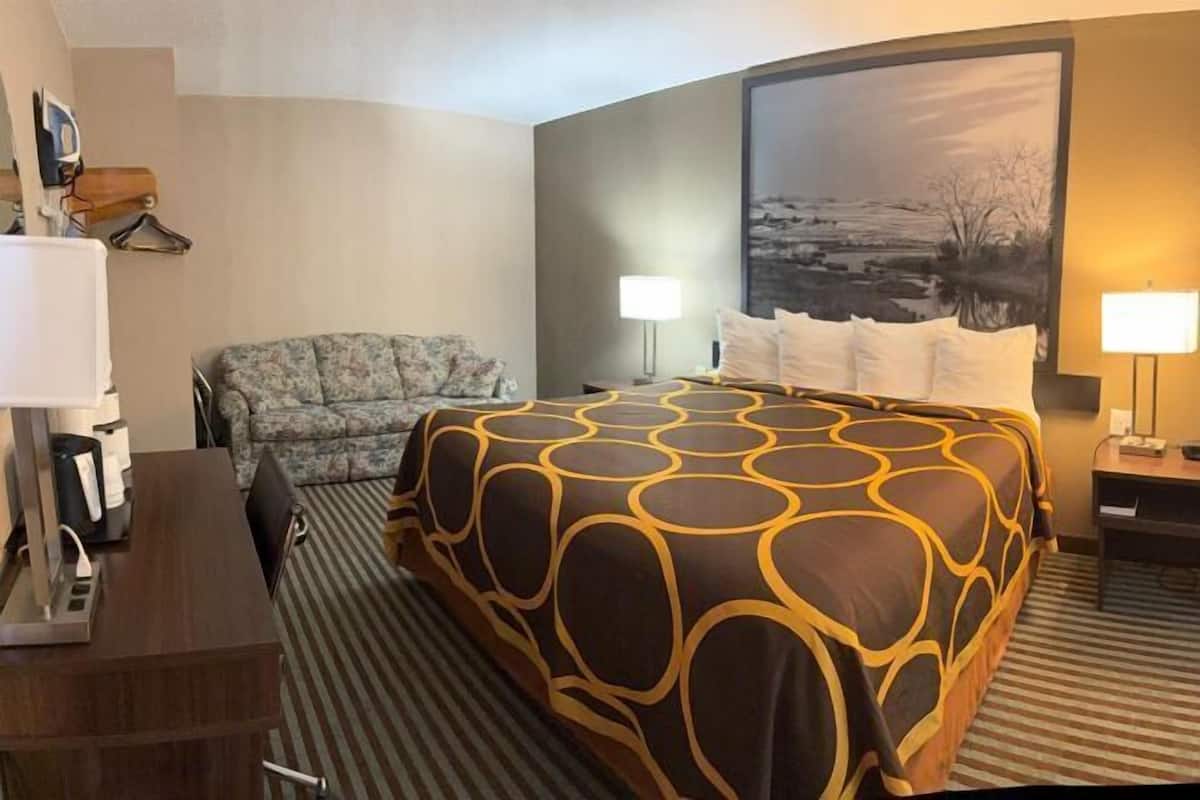 A hotel room with a large bed, a sofa, a desk, and a painting on the wall.