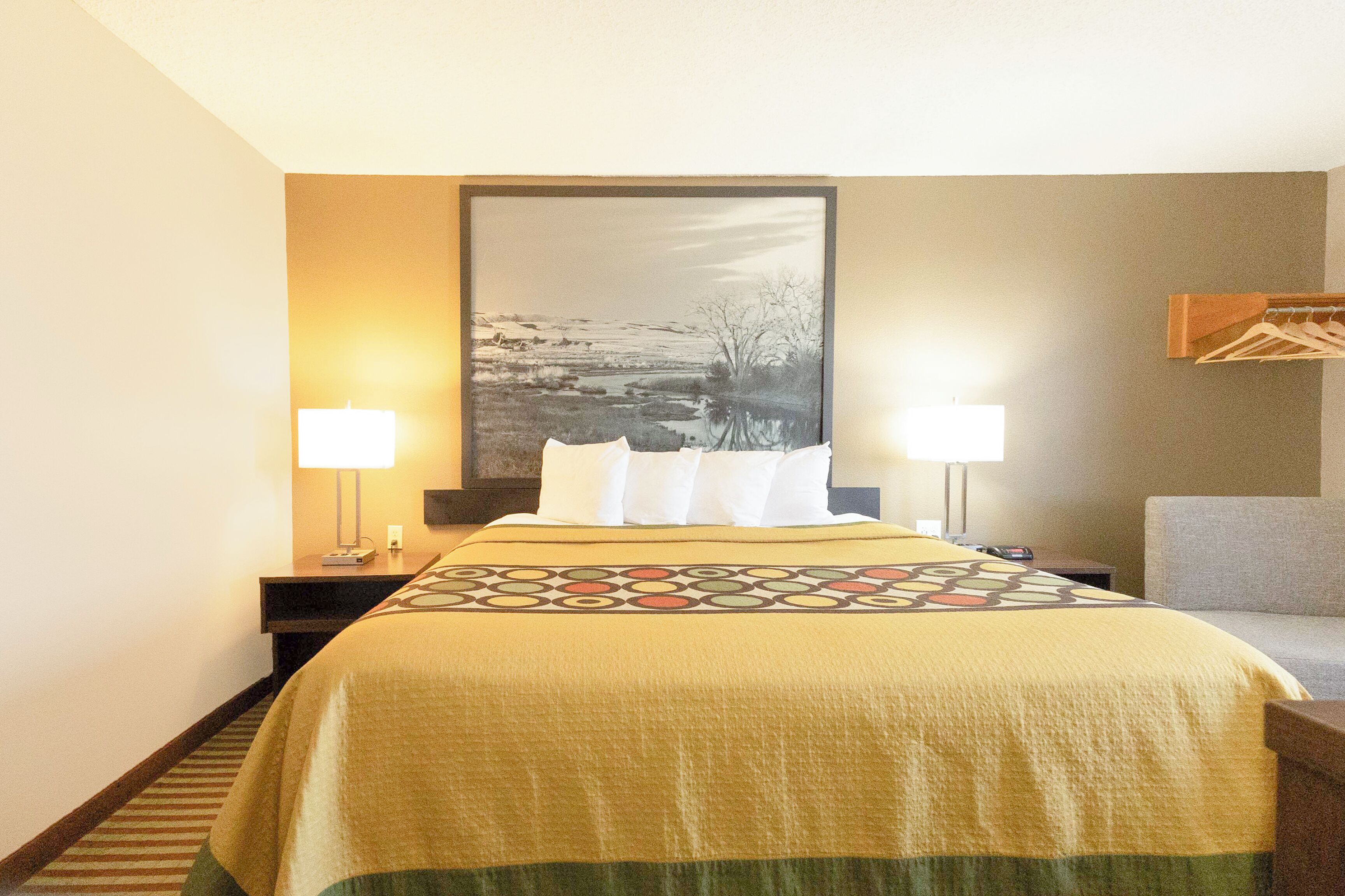 Une chambre d’hôtel avec un lit, deux lampes de chevet, une table de chevet, une chaise et un grand tableau encadré au mur.