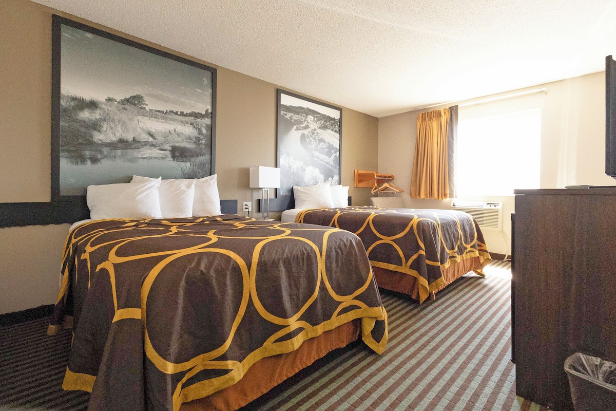 A hotel room with two beds, a large landscape painting, a desk with a chair, and a window with curtains.