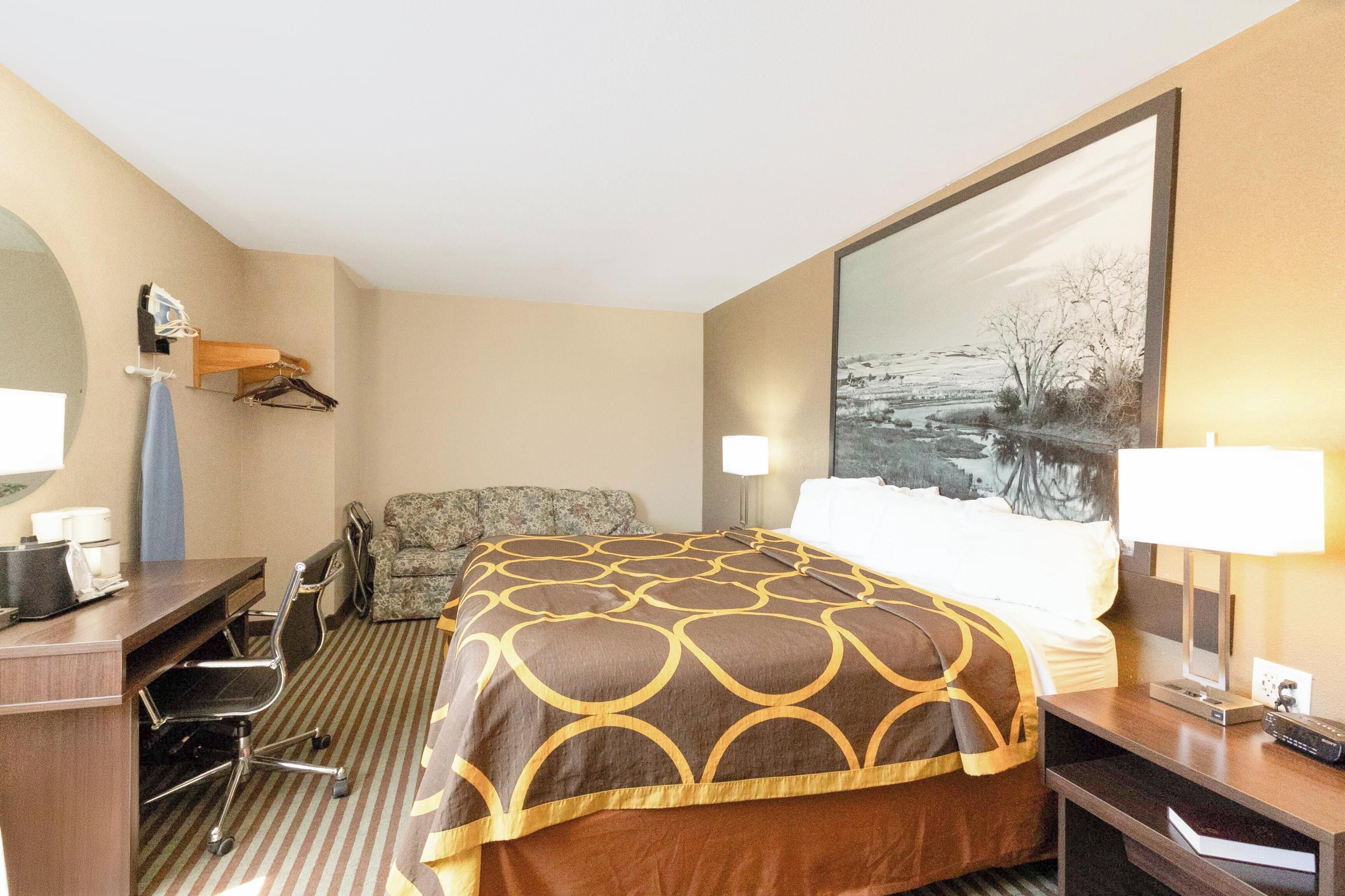 A hotel room with a bed, desk, chair, and a large painting on the wall.