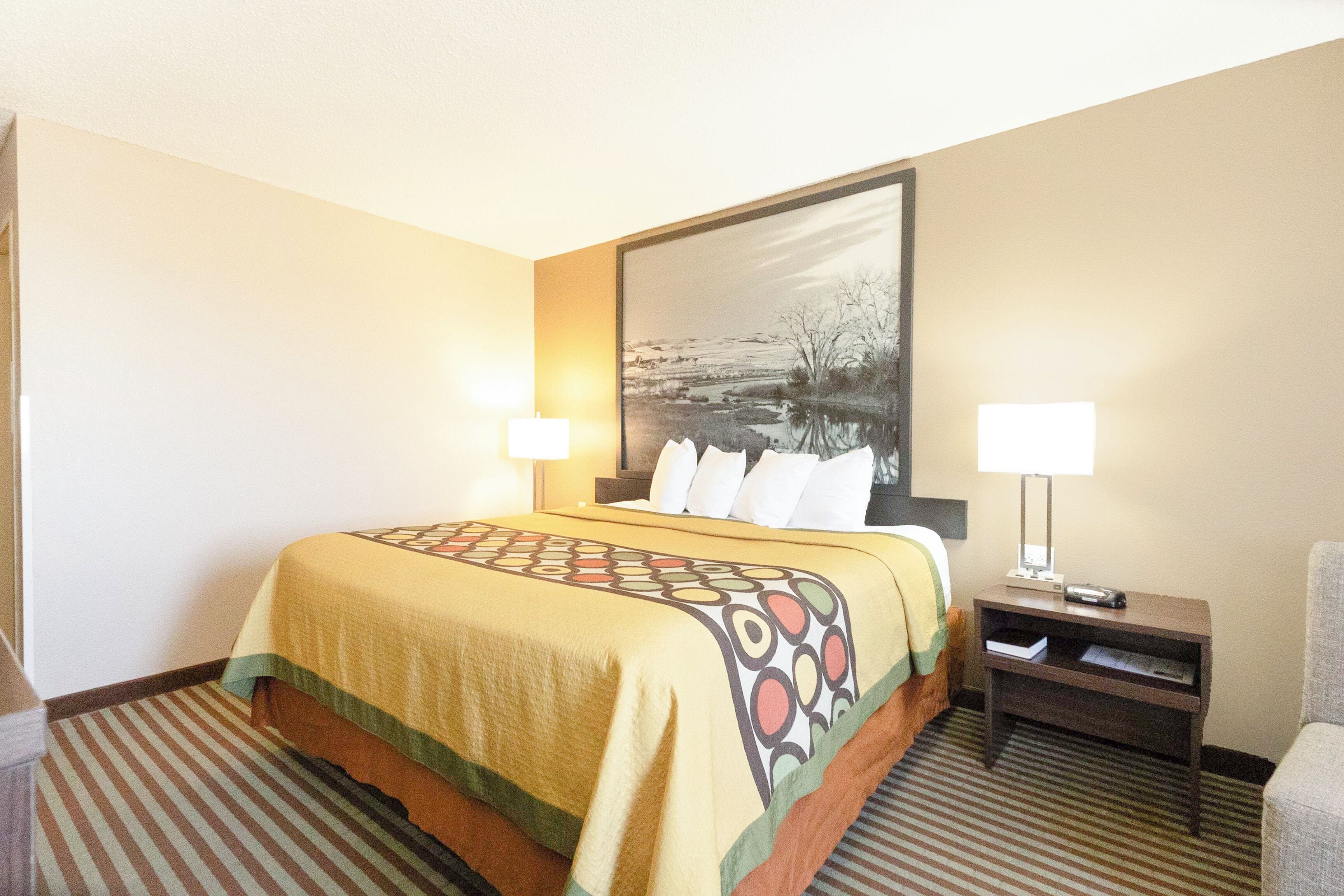 A hotel room with a bed, two bedside lamps, a nightstand, and a framed picture on the wall.