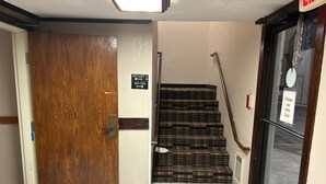 A hotel entrance with a wooden door, a staircase with a checkered carpet, and a sign indicating room numbers 201-227 and 101-125.