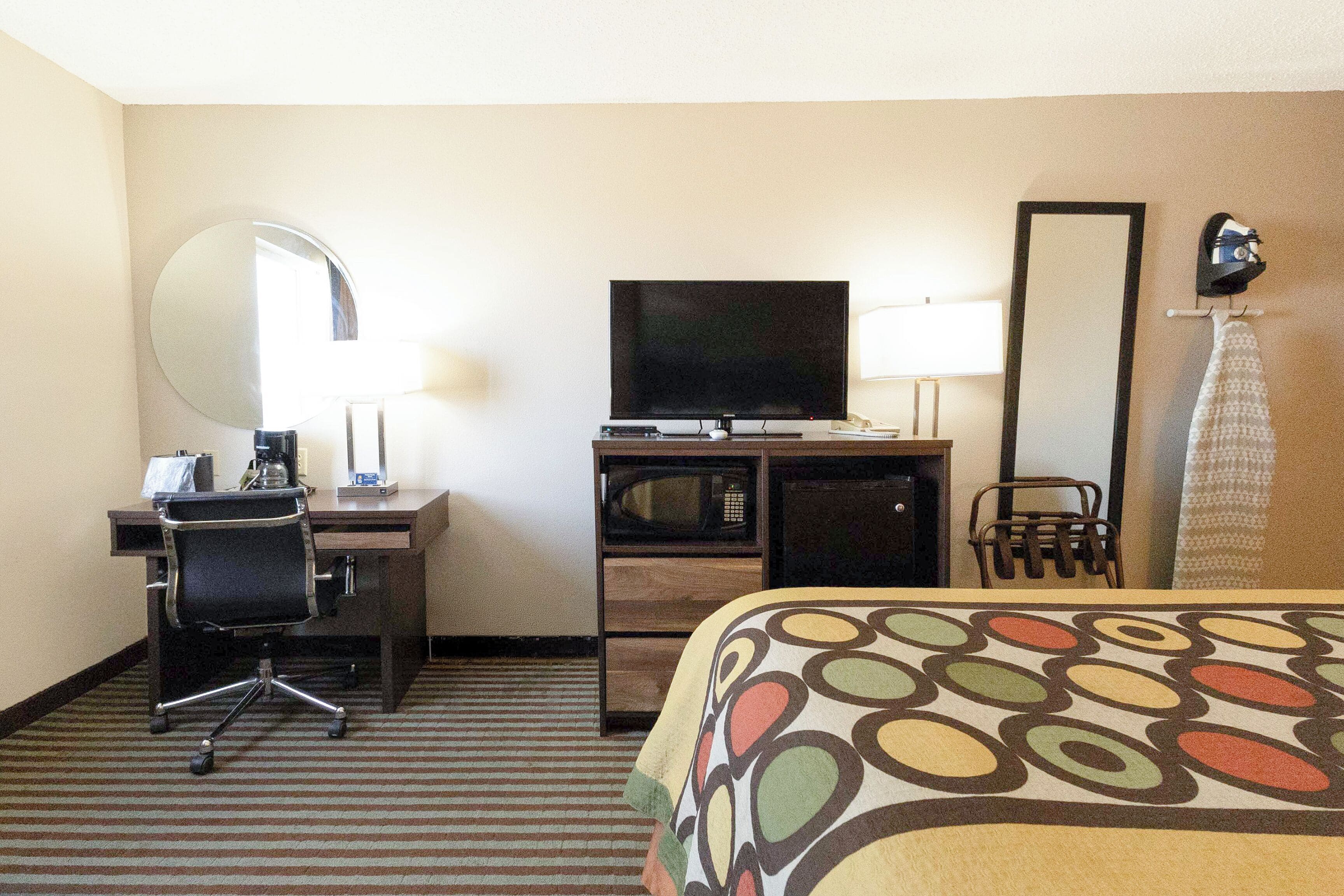 A hotel room with a bed, desk, chair, TV, microwave, and a mirror.