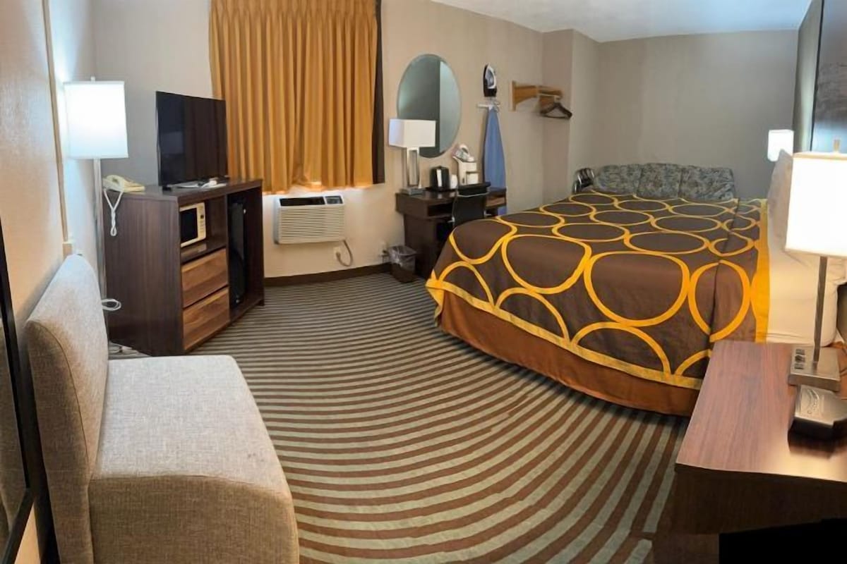 A hotel room with a bed, a desk, a chair, a television, a desk lamp, a mirror, and a window with curtains.