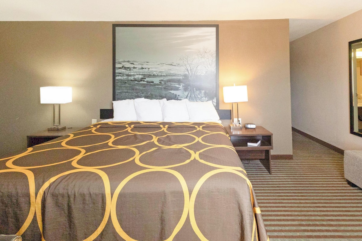 A hotel room with a large bed, two bedside tables, a nightstand, a lamp, and a framed picture on the wall.