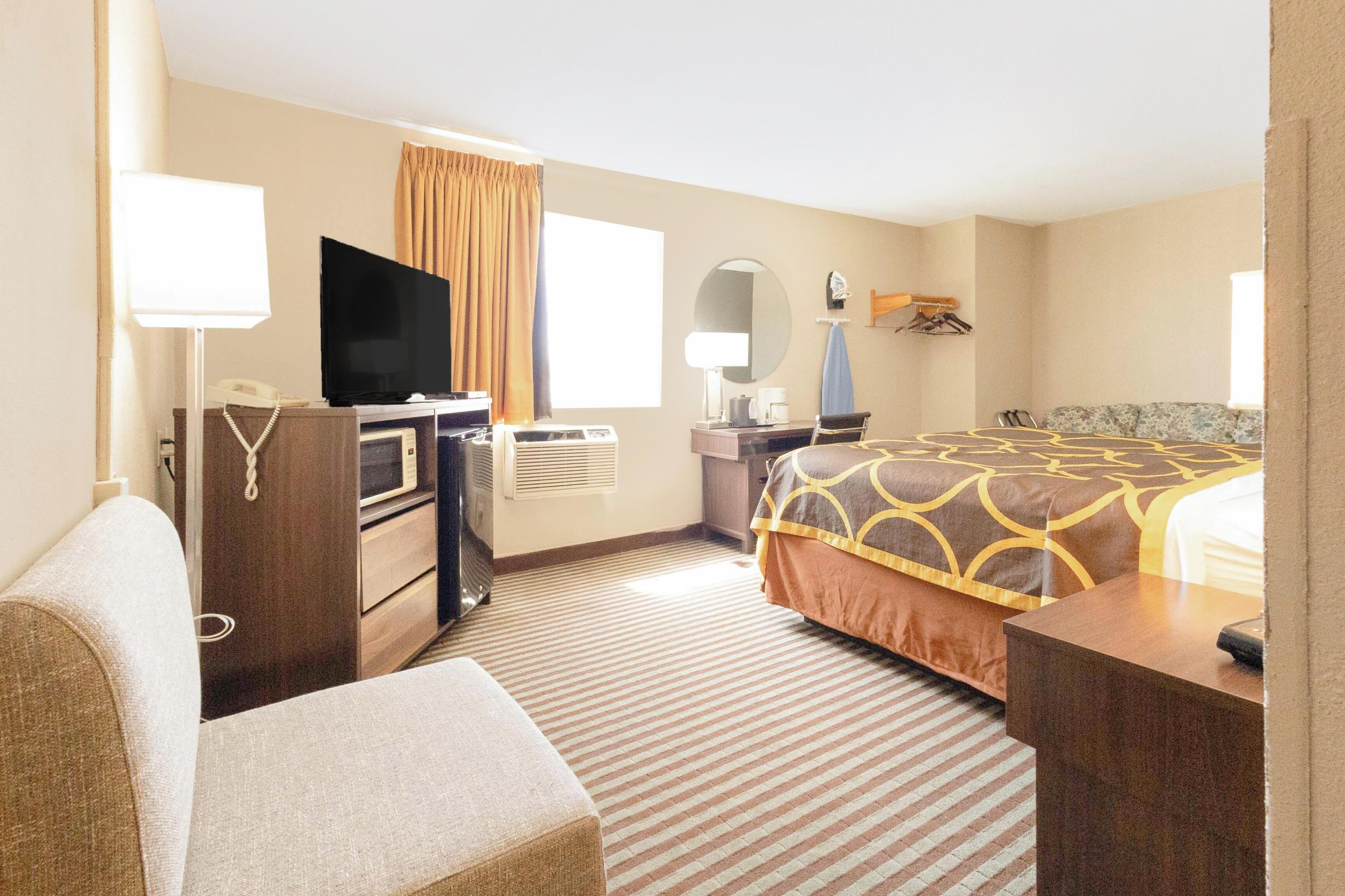 Quarto de hotel com cama, secretária, televisão, candeeiro e espelho.