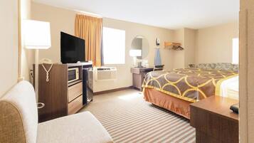 Quarto de hotel com cama, secretária, televisão, candeeiro e espelho.