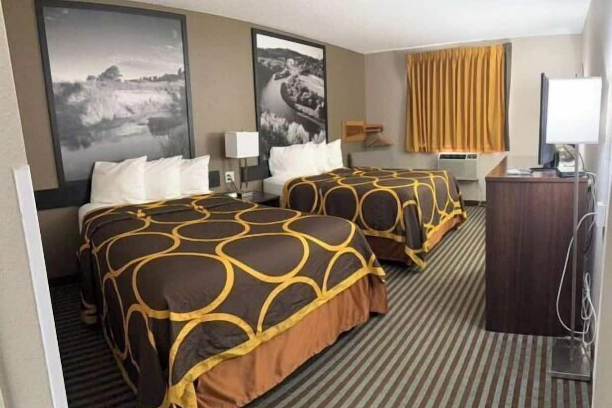 A hotel room with two beds, a desk, a chair, a television, and artwork on the walls.