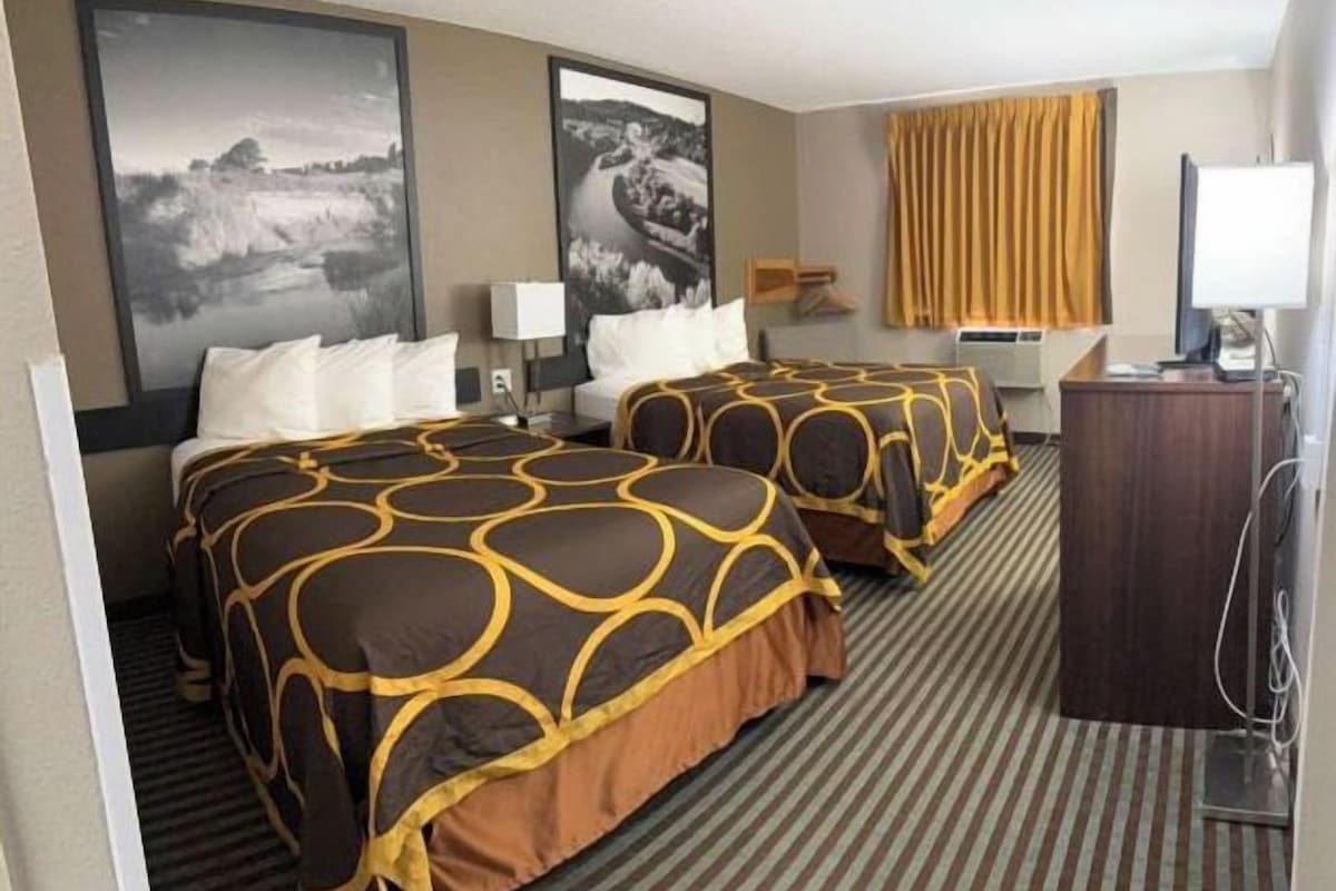 A hotel room with two beds, a desk, a chair, a television, and artwork on the walls.