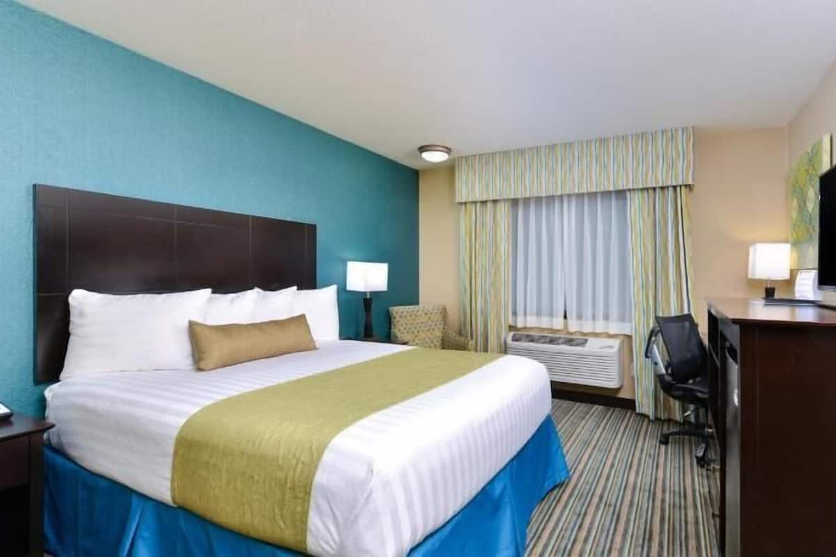 Una habitación de hotel con cama, escritorio, televisión y ventana con cortinas.