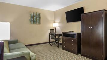 A hotel room with a green sofa, a desk with a lamp, a television on the wall, and a wardrobe.
