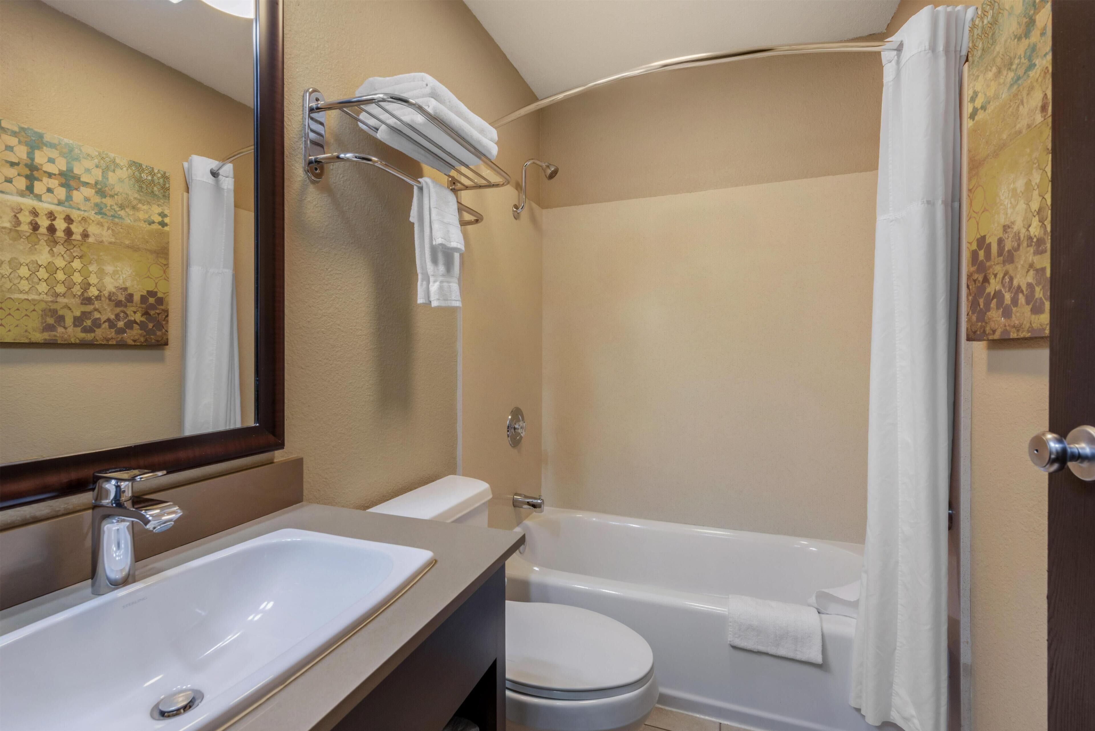 Een badkamer met een wastafel, toilet en bad. Er is een handdoekrek met handdoeken en een douchegordijn.
