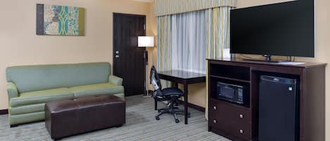 A hotel room with a green sofa, a small desk with a computer, a television, and a microwave.