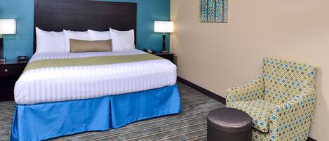 A hotel room with a large bed, a chair, a small table, and a lamp.