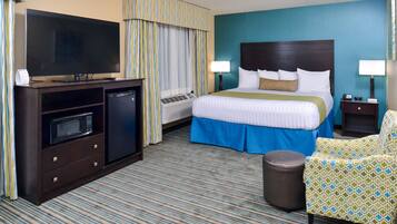 Ein Hotelzimmer mit einem großen Bett, einem Fernseher, einer Mikrowelle, einem kleinen Tisch und einem Sessel.
